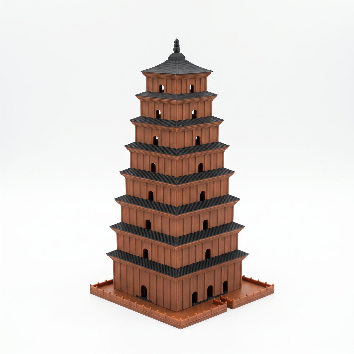 A miniature brown pagoda model with black roofs, standing on a matching brown base against a clean white background.