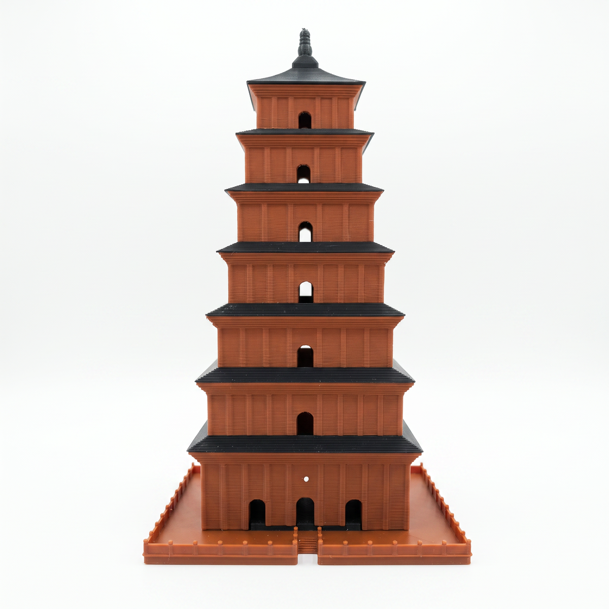 A miniature brown pagoda model with black roofs, standing on a matching brown base against a plain white background.