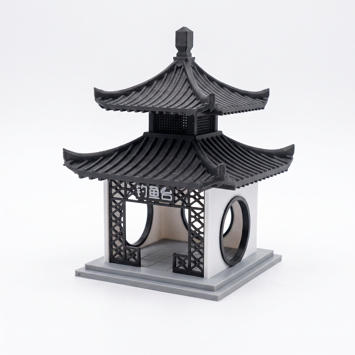 A miniature black and gray pagoda-style decorative structure with curved tiled roofs, lattice side panels, circular openings, and a base, photographed on a clean white studio background.
